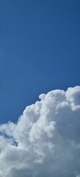 Vertical shot of white fluffy clouds on a blue sky background, can be used for wallpaper