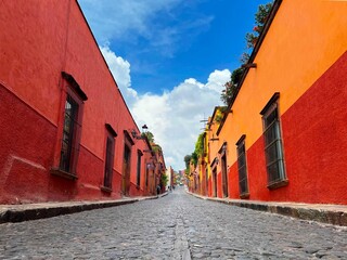 Fototapeta premium Narrow street between traditional buildings under blue cloudy sky in San Miguel de Allende, Mexico