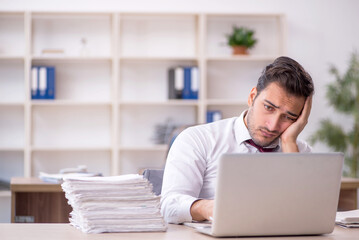 Young male employee and too much work at workplace