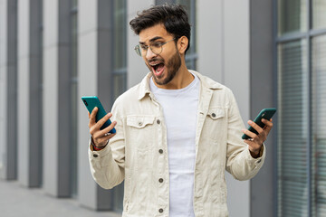 Irritated nervous stressed Indian man talking screaming on two mobile phones having conversation...
