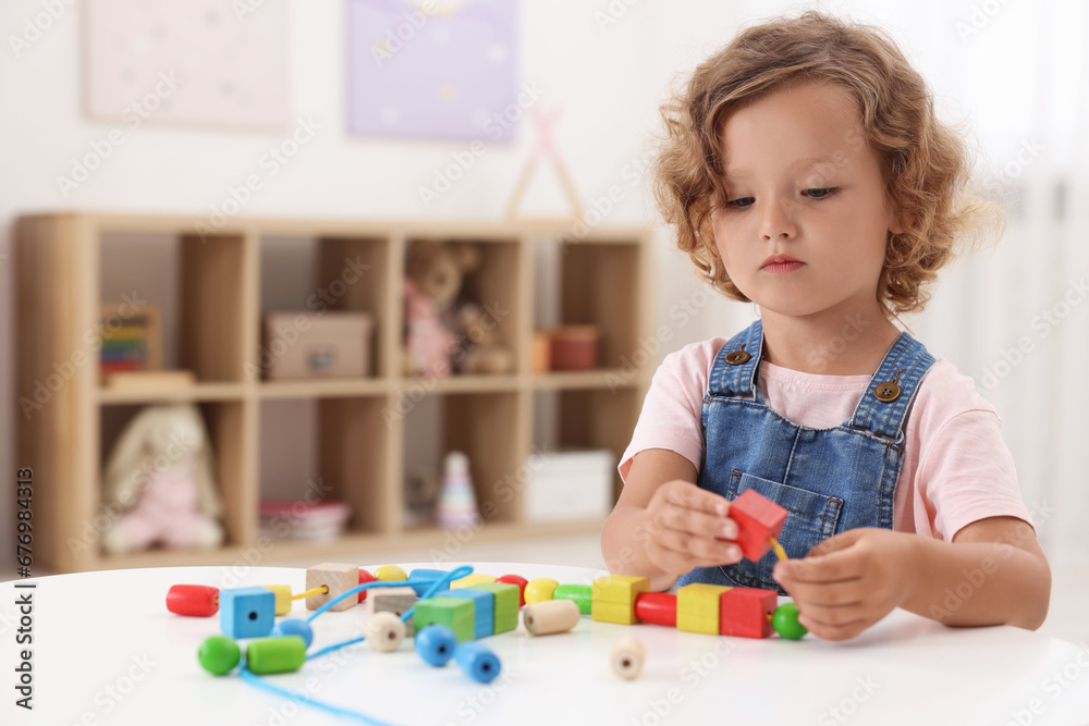 Canvas Prints Motor skills development. Little girl playing with wooden pieces and string for threading activity at table indoors