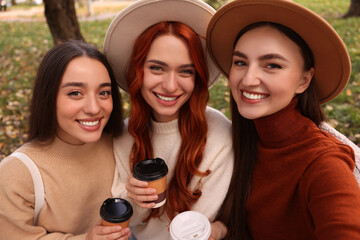 Obraz premium Happy friends with paper cups of coffee taking selfie in park