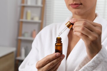 Fototapeta premium Woman with bottle of cosmetic serum and dropper indoors, closeup