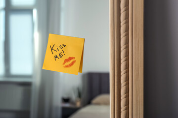 Sticky note with phrase Kiss Me and lipstick mark attached to mirror in room