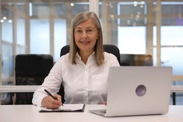 Fototapeta premium Smiling woman with clipboard and laptop working in office. Lawyer, businesswoman, accountant or manager