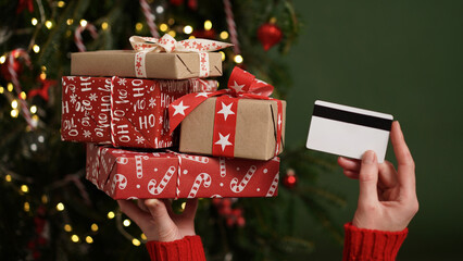 Hands of a woman in a red sweater holding a credit card and a gift box on the background of a...