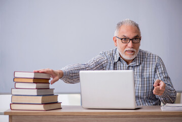 Old male teacher sitting in front of whiteboard