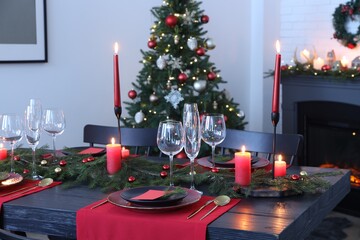 Elegant Christmas table setting with dishware and burning candles in festively decorated room