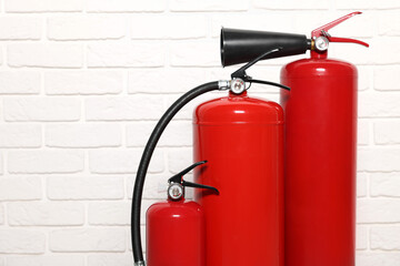 Red fire extinguishers near white brick wall, space for text