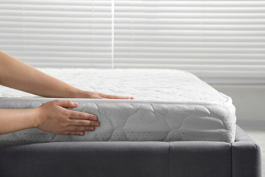 Woman touching soft light green mattress indoors, closeup