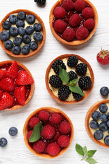 Tartlets with different fresh berries on white wooden table, flat lay. Delicious dessert