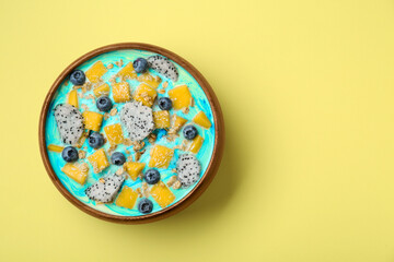 Delicious smoothie bowl with fresh fruits, blueberries and oatmeal on yellow background, top view. Space for text