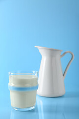 Glass of fresh milk and jug on light blue background
