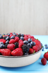 Different fresh ripe berries on light blue wooden table. Space for text