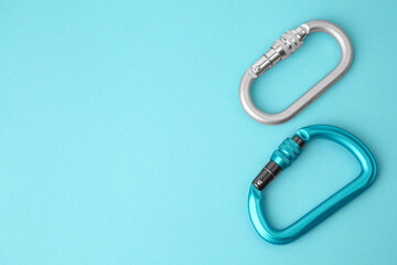 Fototapeta premium Two metal carabiners on light blue background, flat lay. Space for text