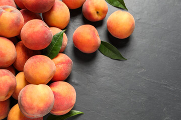 Fresh peaches and leaves on dark grey textured table, flat lay. Space for text