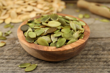 Bowl with peeled pumpkin seeds on wooden table, closeup