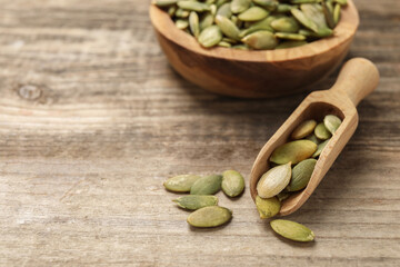 Scoop and bowl with peeled pumpkin seeds on wooden table, closeup. Space for text