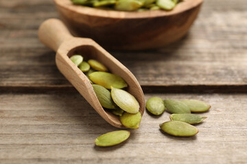 Scoop with peeled pumpkin seeds on wooden table, closeup