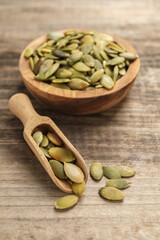 Bowl and scoop with peeled pumpkin seeds on wooden table