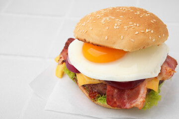 Delicious burger with fried egg on white tiled table, closeup. Space for text