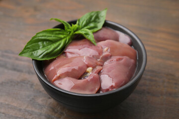 Bowl of raw chicken liver with basil on wooden table, closeup