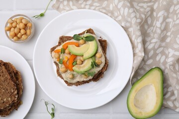 Tasty vegan sandwich with avocado, chickpeas and bell pepper on white tiled table, flat lay