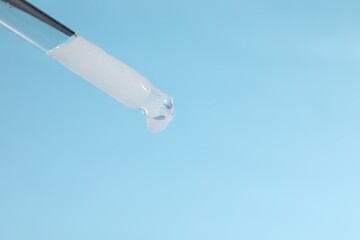 Dripping cosmetic serum from pipette on light blue background, closeup. Space for text