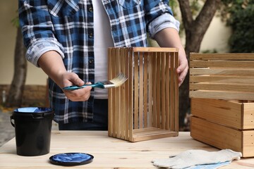 Man applying varnish onto wooden crate at table outdoors, closeup - obrazy, fototapety, plakaty