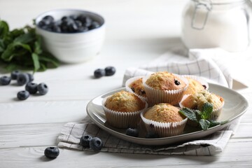 Delicious sweet muffins with blueberries and mint on white wooden table. Space for text