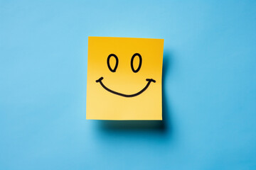Positive attitude concept, happy hand drawn yellow color sticky note, smiling sticky note paper isolated in blue background.