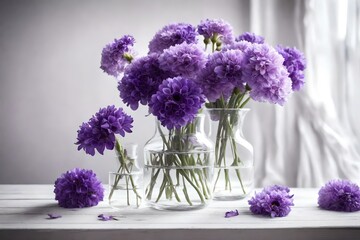 On a white wooden table, there are purple flowers in a transparent glass vase