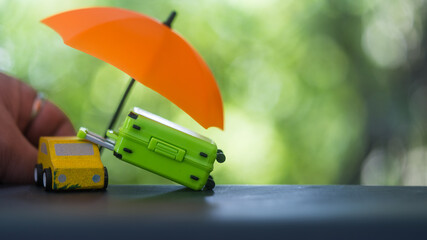 An orange umbrella covers a green suitcase and a yellow car. Travel insurance, accidents and...