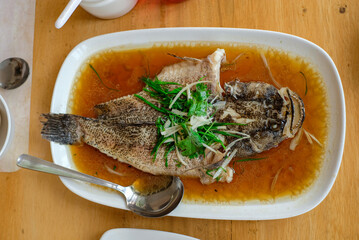 steam fried Marbled Goby fish called Ikan Malas in siamese style served in a dish on a wooden table in a restaurant in Indonesia