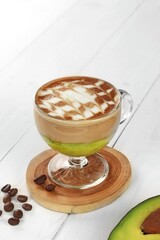 iced avocado coffee, fresh blended avocado poured one shot of espresso in a plastic cup on a wooden coaster