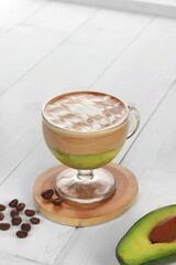 iced avocado coffee, fresh blended avocado poured one shot of espresso in a plastic cup on a wooden coaster