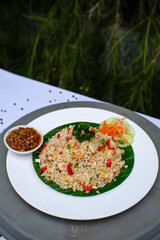 fried rice with vegetables, chicken and chili sauce is served on a white plate on the table