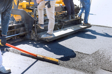 Pavement machine laying fresh bitumen asphalt on top of gravel base during highway construction