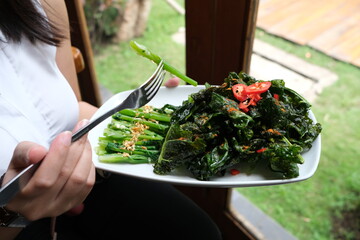 fried cooked green vegetables called kailan served on a restaurant dining table using a white plate - obrazy, fototapety, plakaty