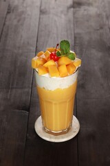 yellow mango juice with garnish of mango pieces, cherries and mint leaves. with a white background and dark wood