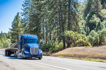 Fototapeta na wymiar Bonnet powerful big rig semi truck tractor transporting fastened cargo on flat bed semi trailer driving on the multiline highway road