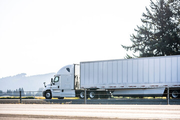 Popular model of the big rig white semi truck transporting cargo in dry van semi trailer running on...