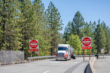 Powerful big rig semi truck transporting liquid cargo in tank semi trailer running from highway...