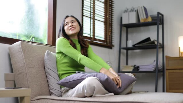 Young Asian woman at home doing stretches to relax while sitting on the sofa in the living room on vacation. Girl resting in the house.