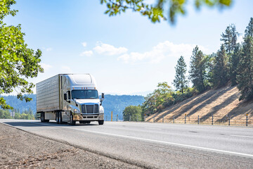 Fototapeta na wymiar Work horse big rig semi truck transporting cargo in loaded refrigerator semi trailer driving on the mountain highway road in California