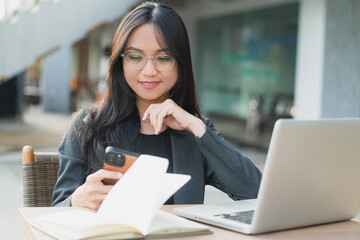 Young confident businesswoman using her smart phone while sitting at the office desk.