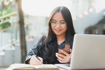 Young confident businesswoman using her smart phone while sitting at the office desk.