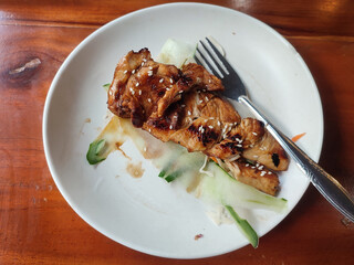 Teriyaki chicken on a white plate on a wooden table.  Flat lay, negative space.