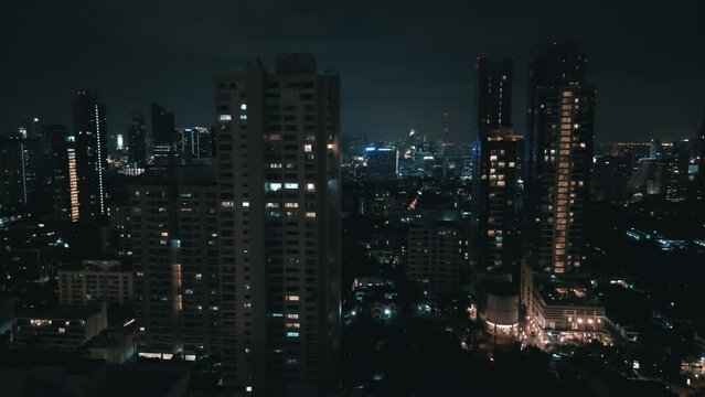 Beautiful aerial panorama of night Bangkok at nighttime. Camera moving up high between skyscrapers showing lights of the night city with modern buildings and streets, aerial drone shot of night city.