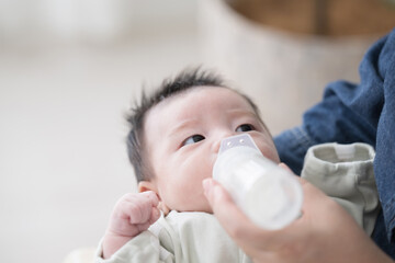  Baby in baby clothes drinking milk from a bottle, overhead view on back while being held by mom